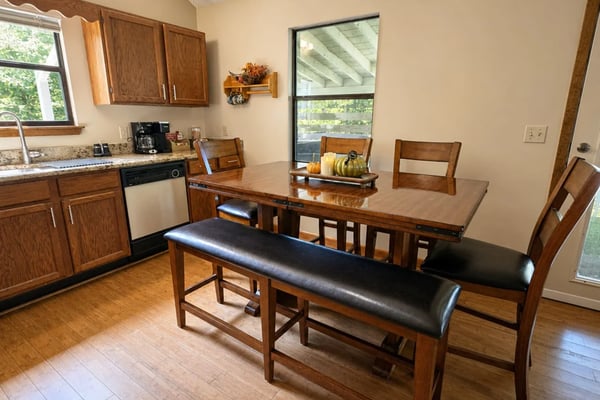 Kitchen and dining area with wood cabinets, granite countertop, dining table with bench seating, and large windows overlooking trees